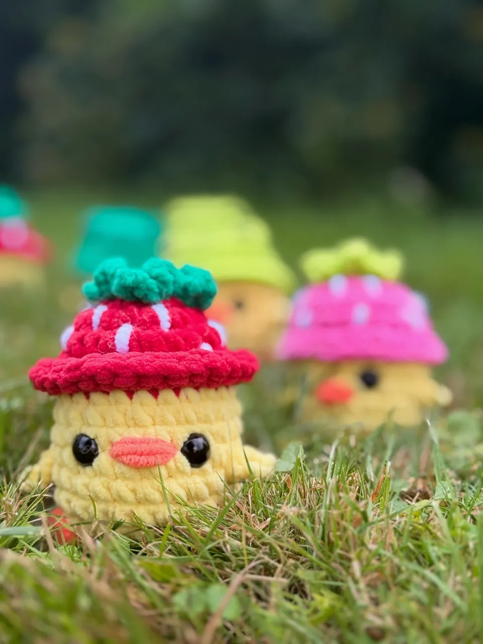 Crocheted chicks in the grass wearing various hats like mushrooms and turtles