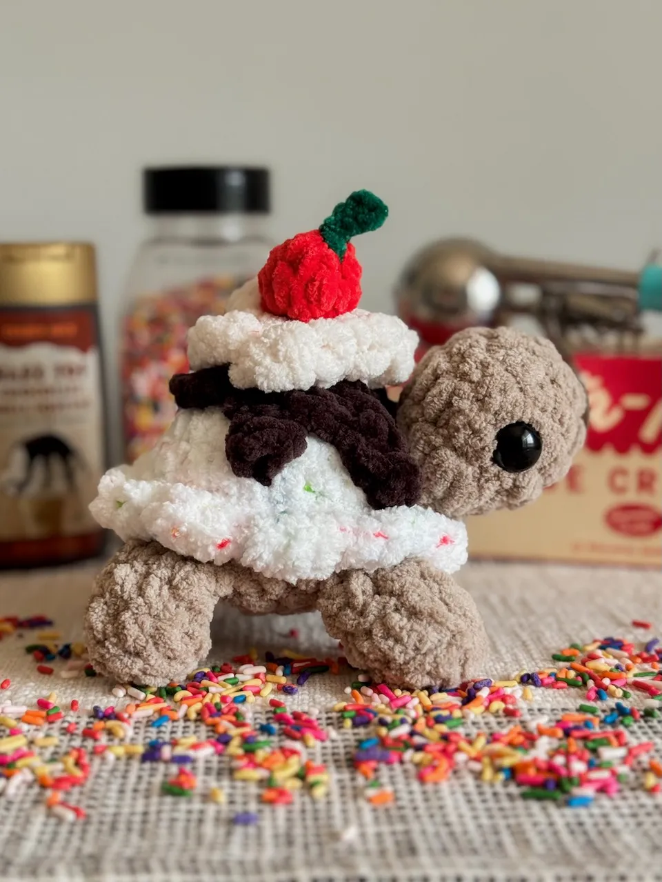 Crocheted turtle with an ice cream cone on its back standing in a pile of sprinkles